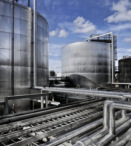 Close-up of industrial piping and storage tanks used in crude oil processing with field instrumentation and control equipment.